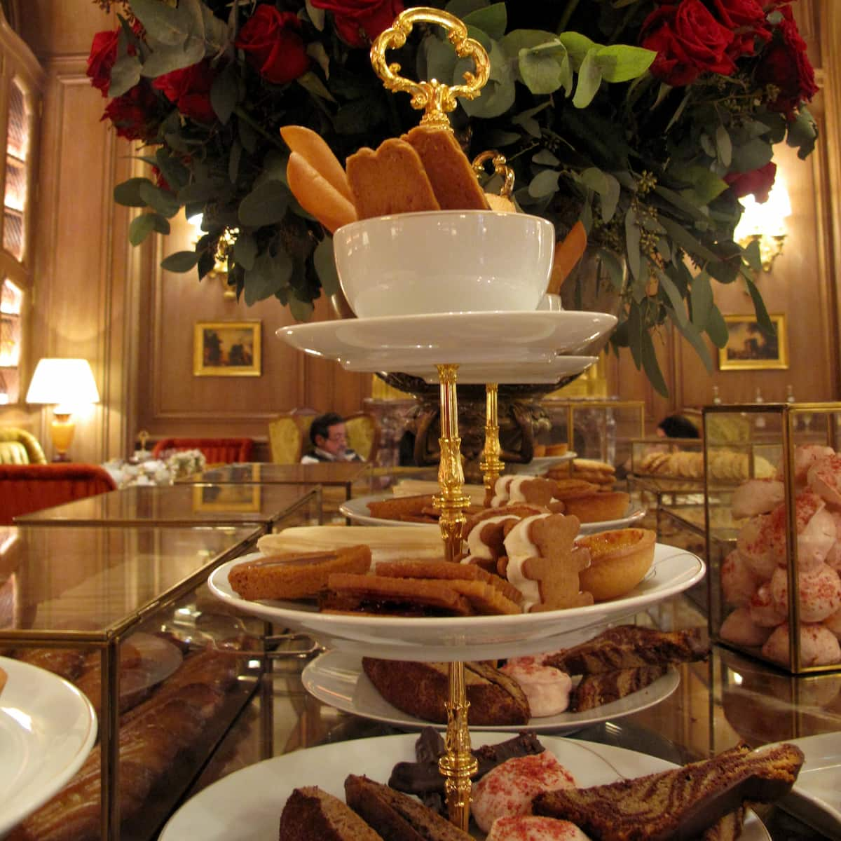 cake stand with various biscuits and cakes beside red roses on a marble and glass table