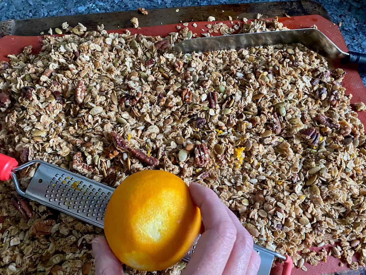 zesting an orange on top of baked crispy granola on a baking tray