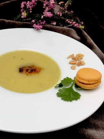 large rimmed porcelain bowl of creamy soup with a mini macaron as decor