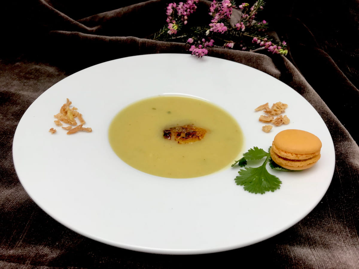 large rimmed white bowl of curried cauliflower soup garnished with a curry macaron