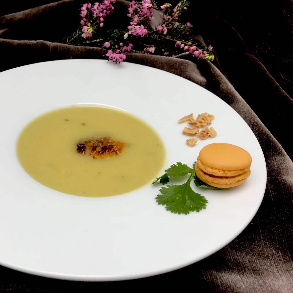 large rimmed porcelain bowl of creamy soup with a mini macaron as decor