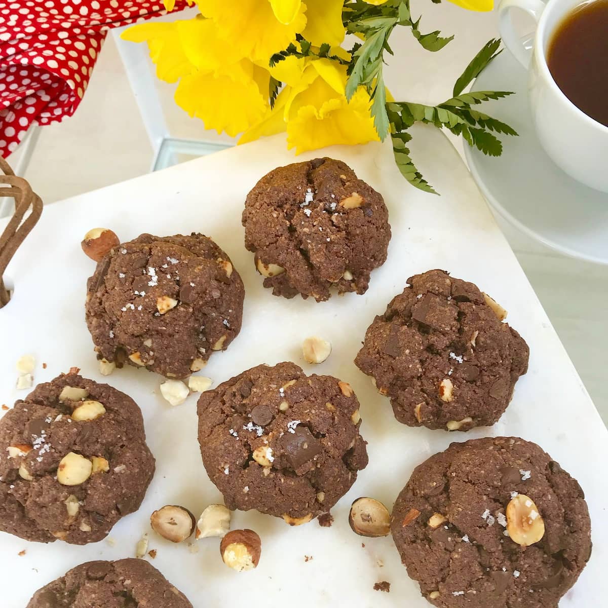 chocolate cookies on white plate with toasted broken hazelnuts and cup of tea