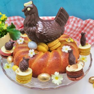 lemon drizzle cake for Easter shaped like a nest topped with chocolate hen, macarons and eggs