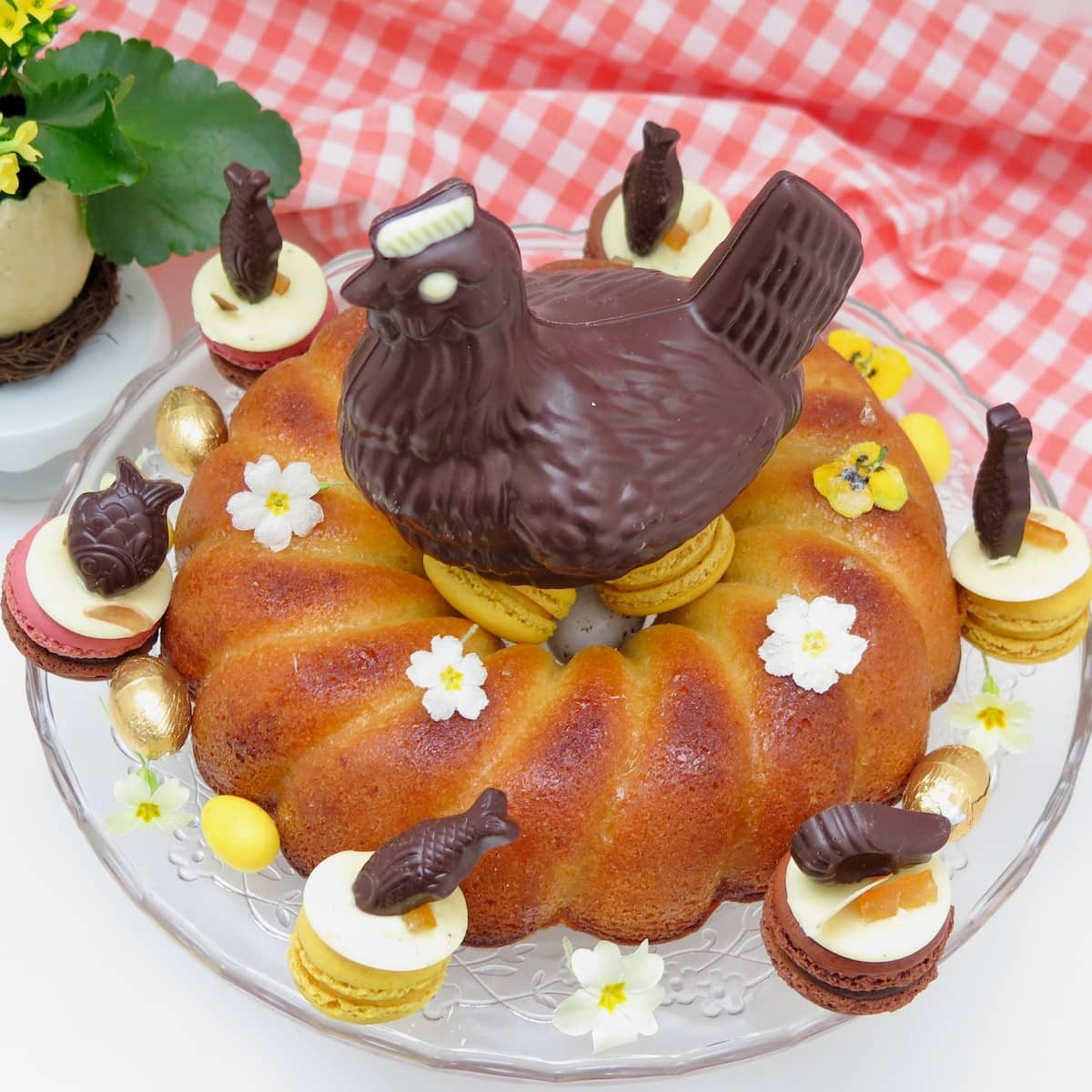 arial view of chocolate hen sitting on a gluten free easter cake with lemon drizzle and decorated with eggs and  lemon macarons