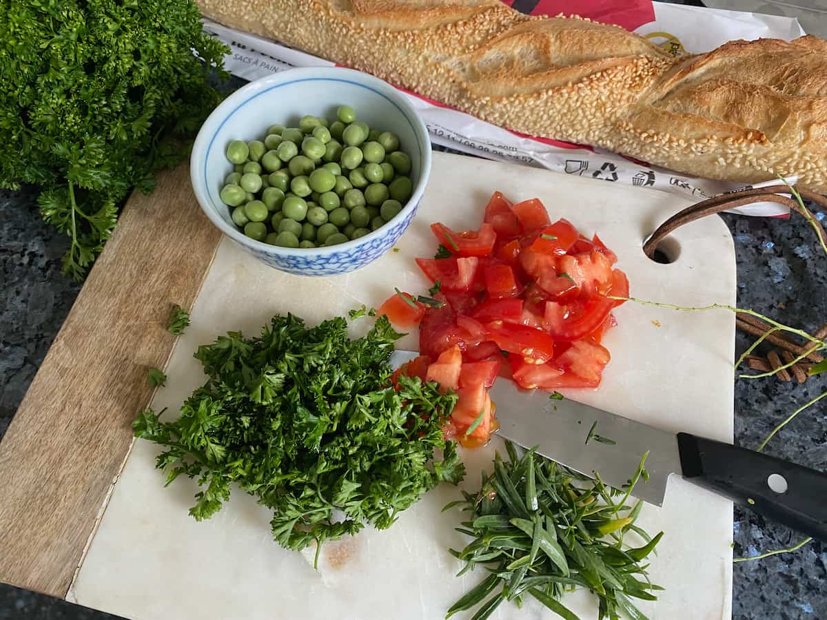 chopped tomatoes, shelled peas and chopped herbs on a board
