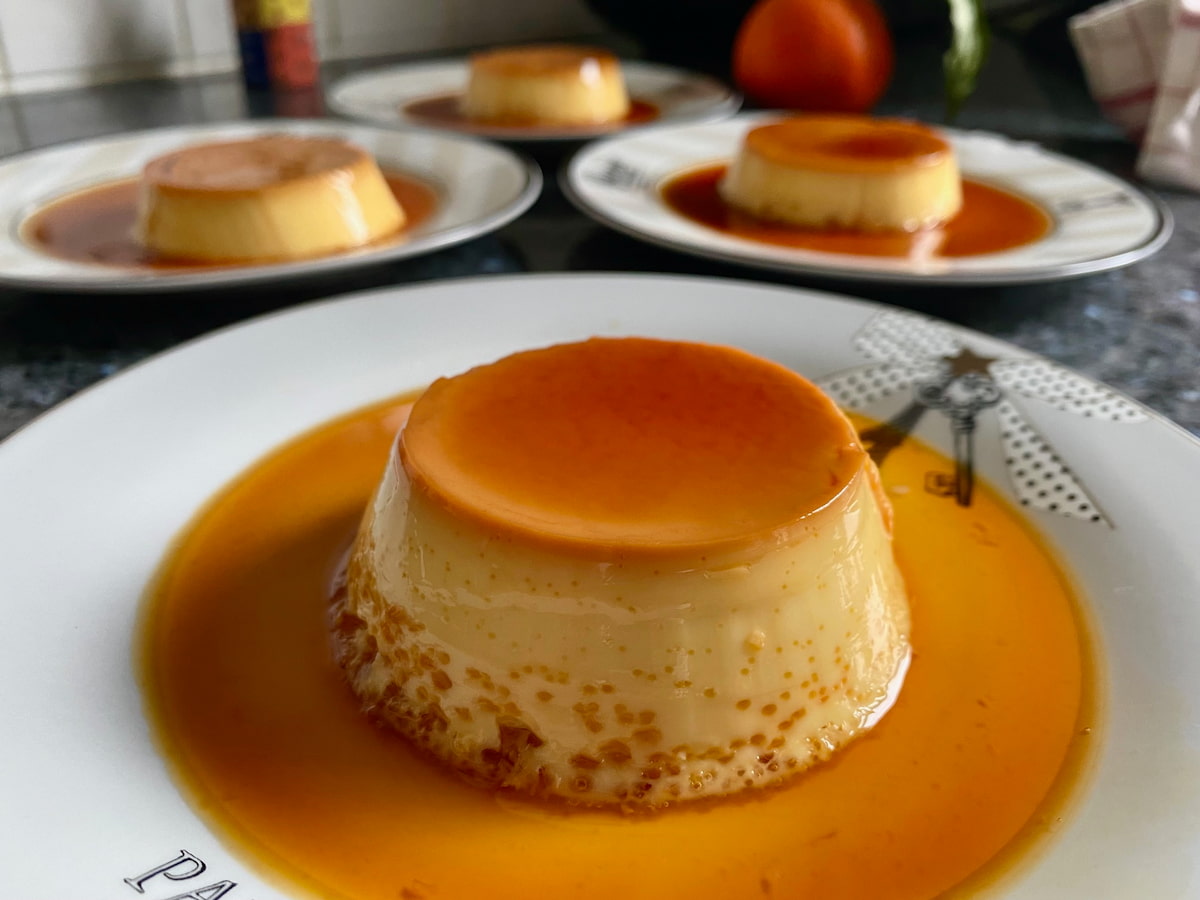 shiny creme caramel with some bubbles, showing it's slightly overcooked - sitting in a pool of caramel sauce