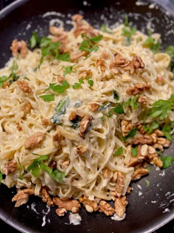 pan of fresh pasta noodles with goat cheese sauce, parsley and walnuts