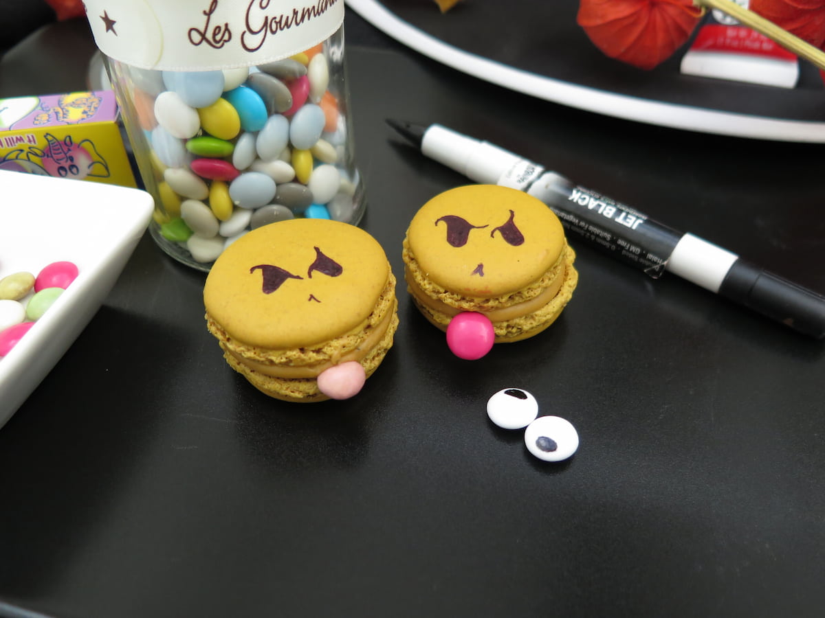 2 green macarons with eyes and smarties as tongues