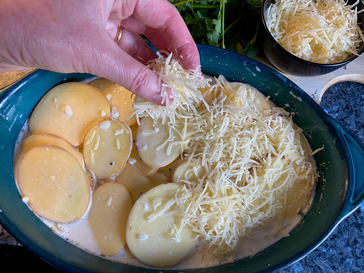 sprinkling grated white cheese over a gratin dish of sliced potatoes and cream 