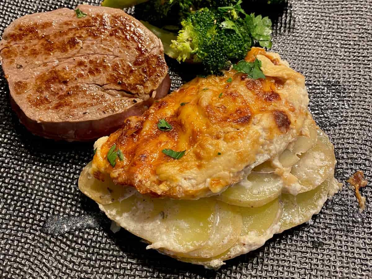 portion of potato bake or cheesy gratin served with a tournedos steak and broccoli