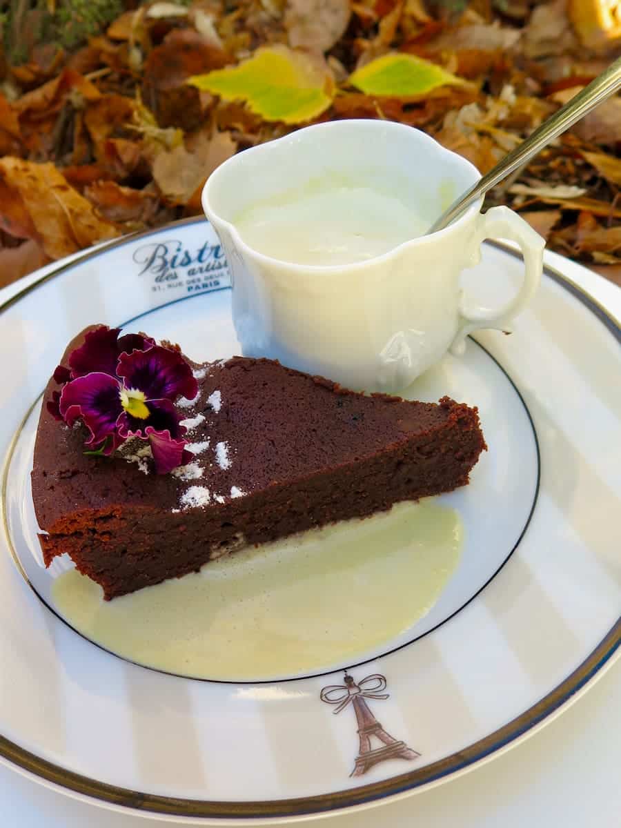 slice of chocolate cake surrounded by thin custard and more sauce in a cup