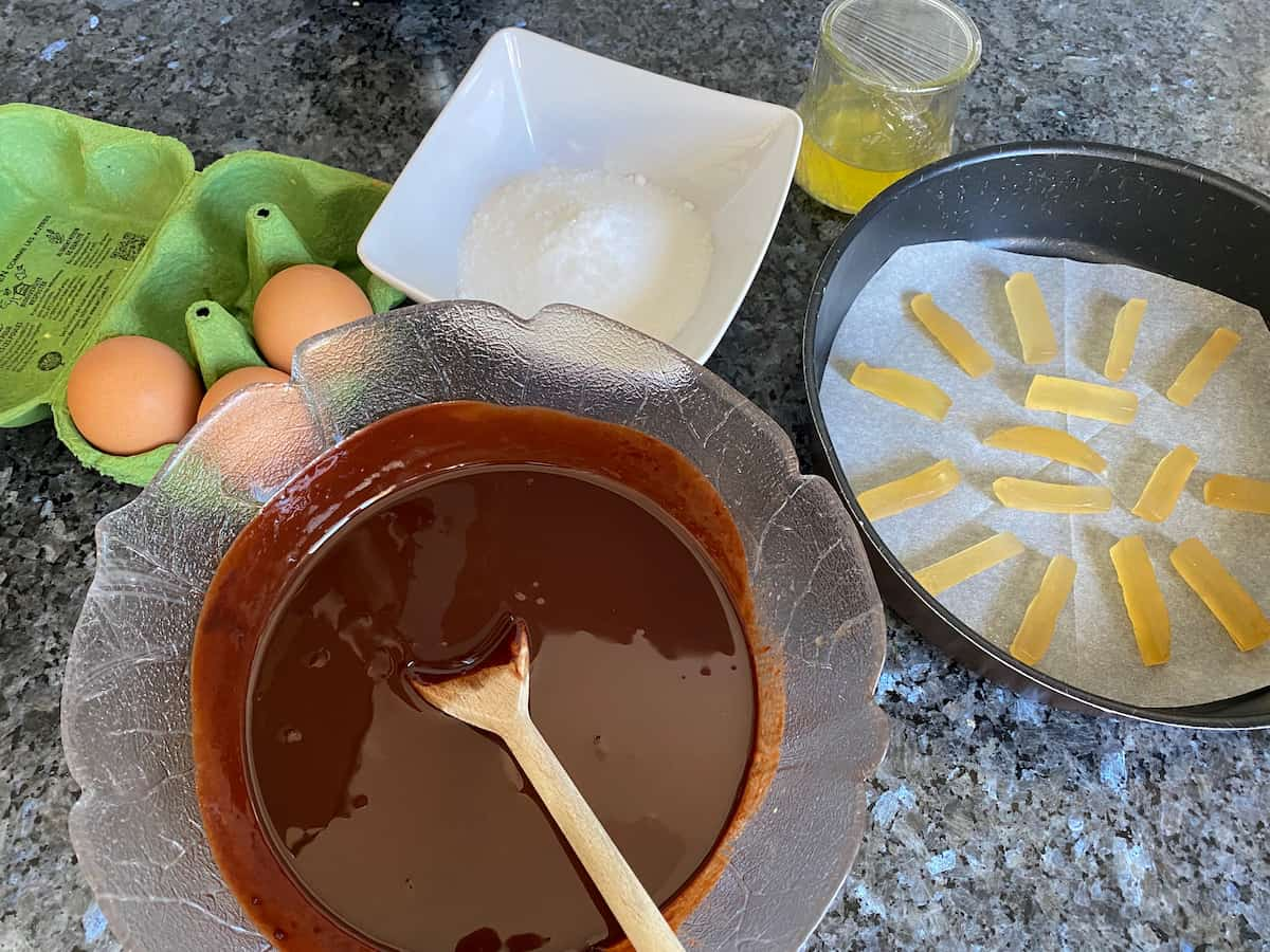 bowl of melted chocolate, cake tin lined with candied ginger and other ingredients around it