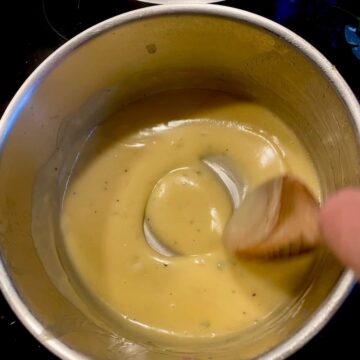 stirring a thick, glossy light yellow sauce in a pan