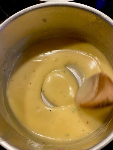 stirring a thick, glossy light yellow sauce in a pan