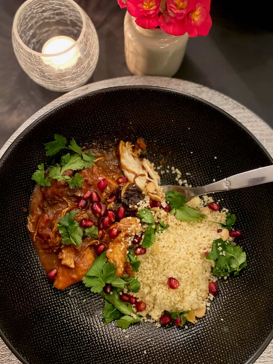 large black bowl containing a stew, semolina with green coriander leaves and bright red pomegranate seeds