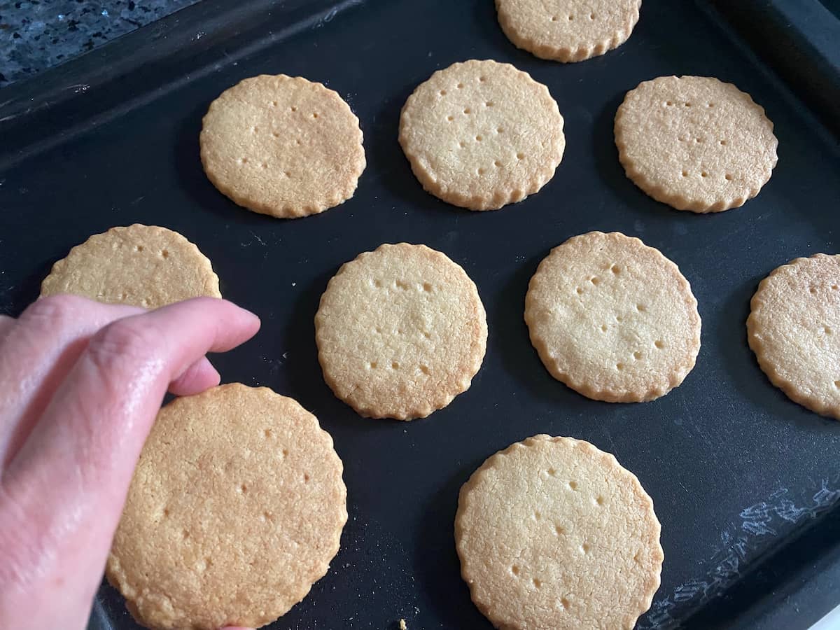 taking a golden round shortbread cookie off the baking tray