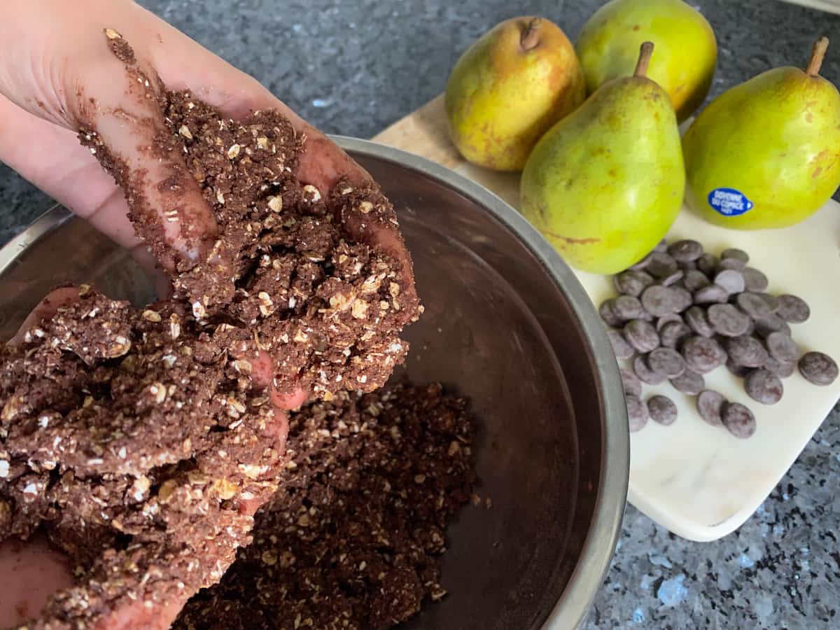 fingers rubbing chocolate, oats, flour, butter and sugar to make a crumble topping