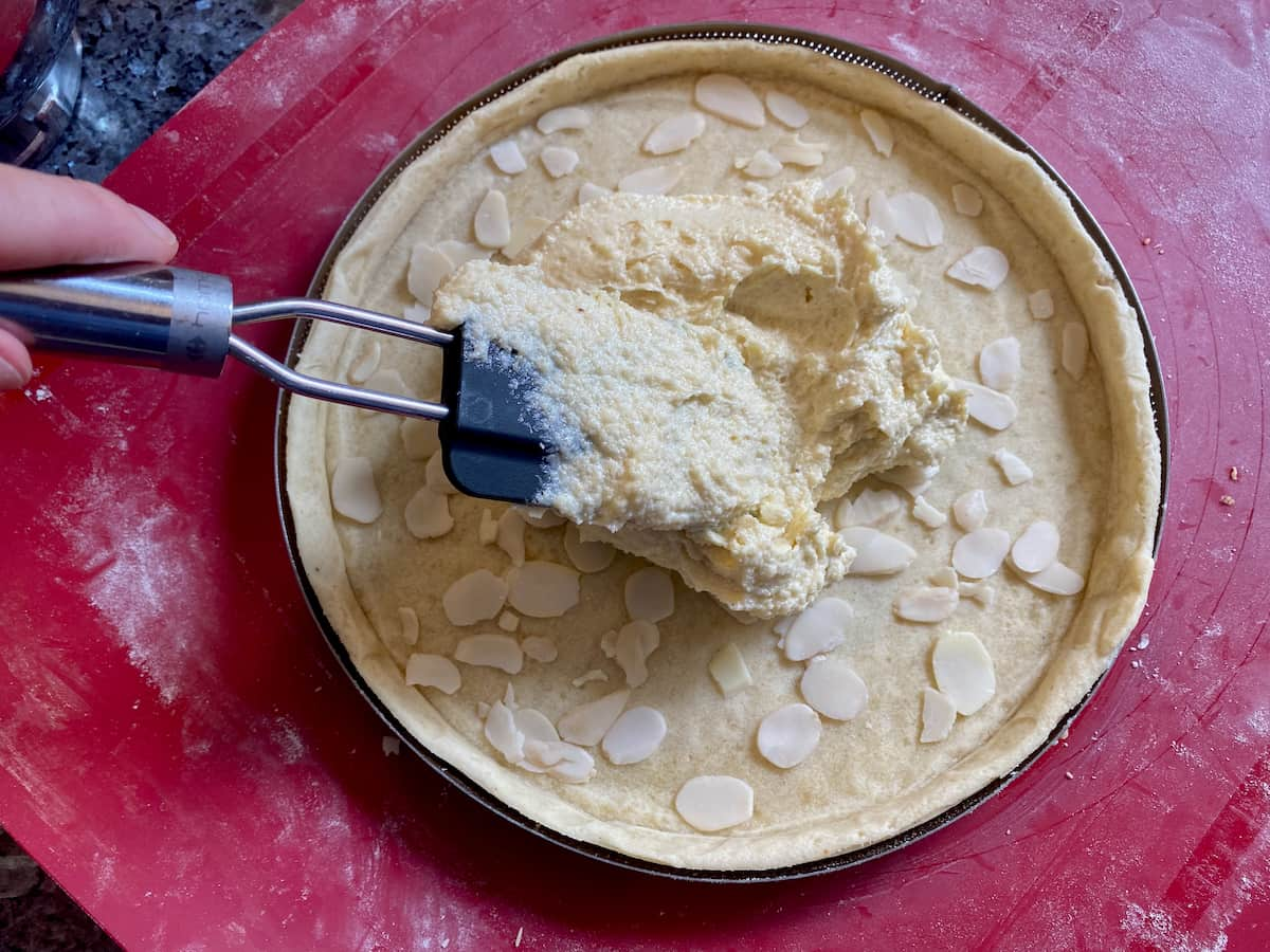 spreading an almond filling into a tart base with slivered almonds