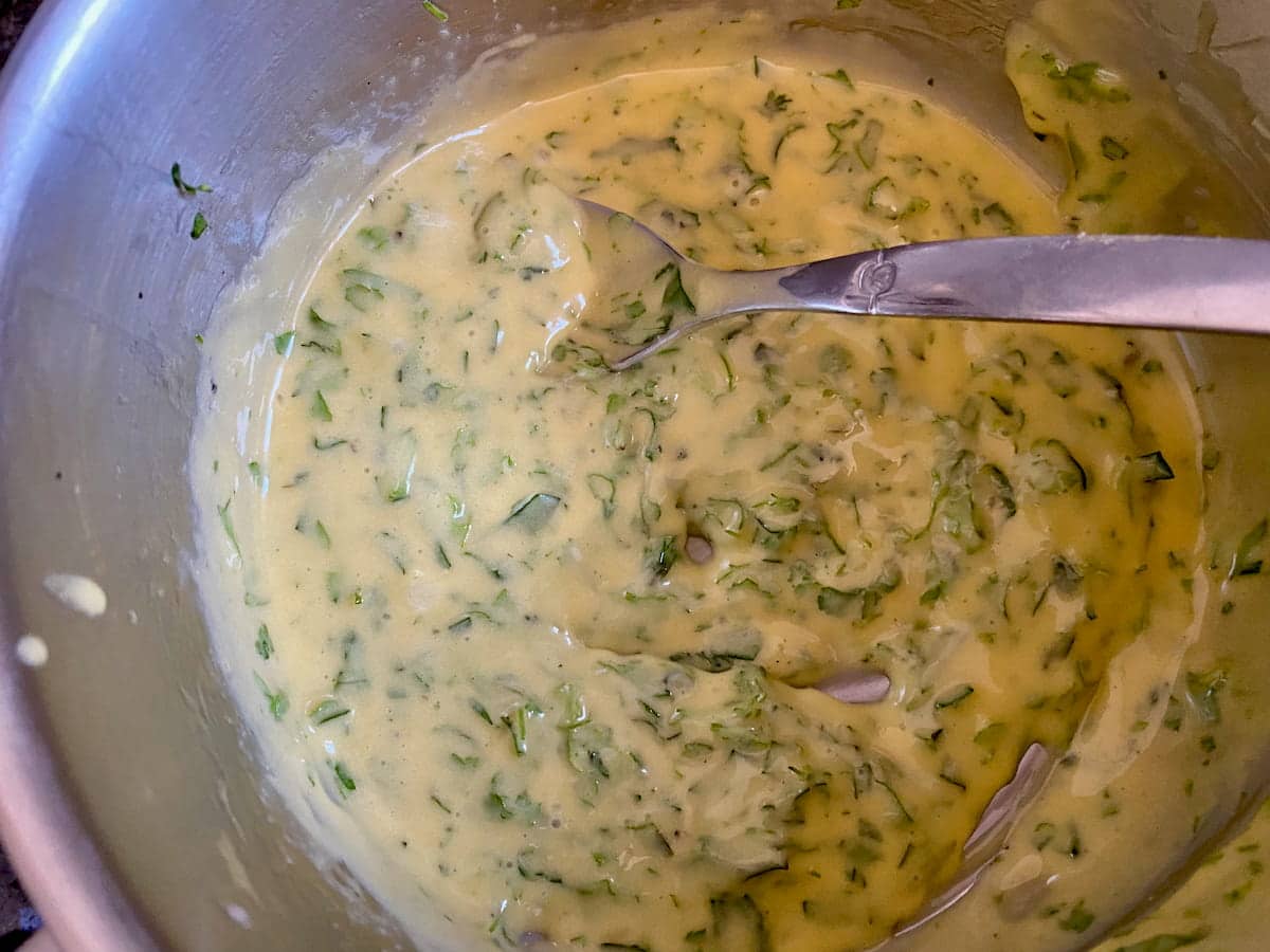 stirring creamy sauce with chopped herbs in a saucepan