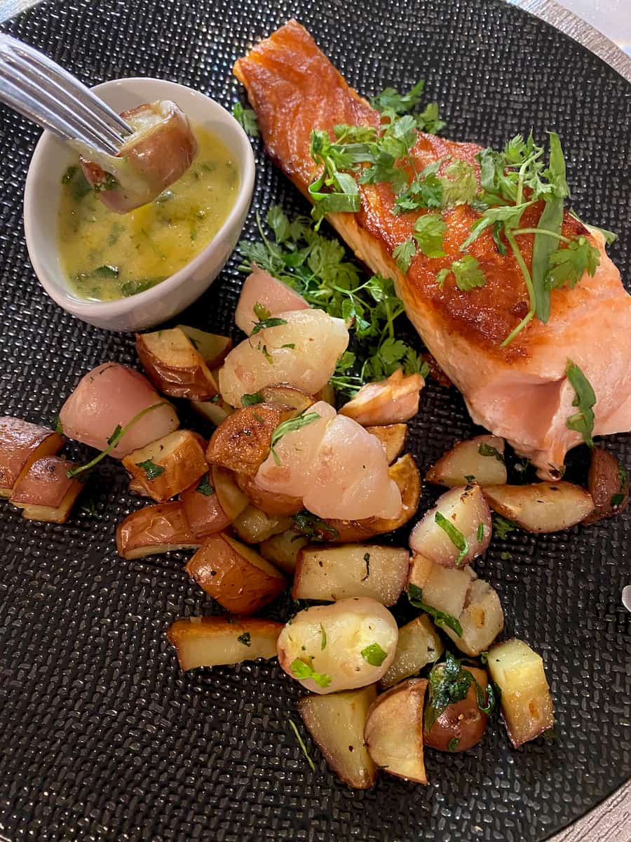 dipping a forked potato into a bowl of creamy, herby sauce on a plate of perfectly cooked salmon and potatoes