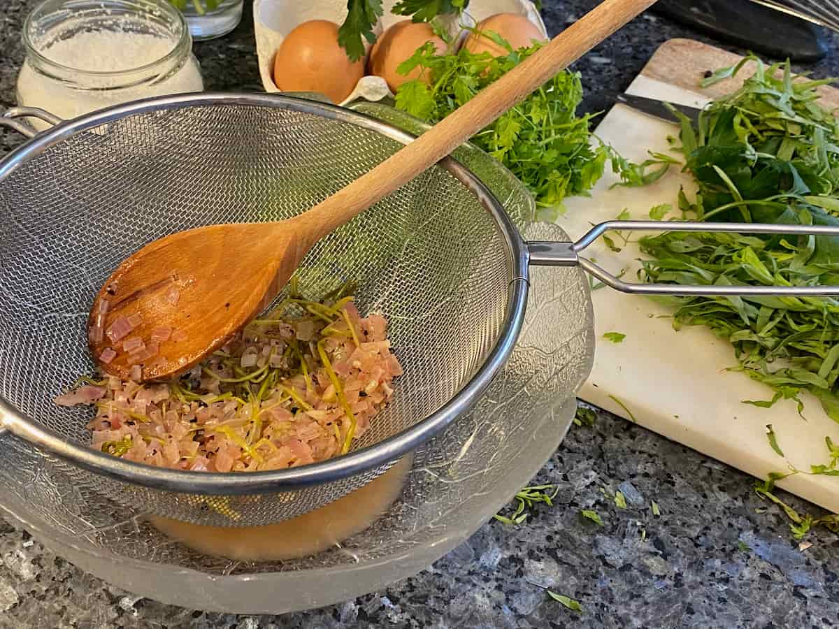 sieving out shallots and herbs for a liquid reduction