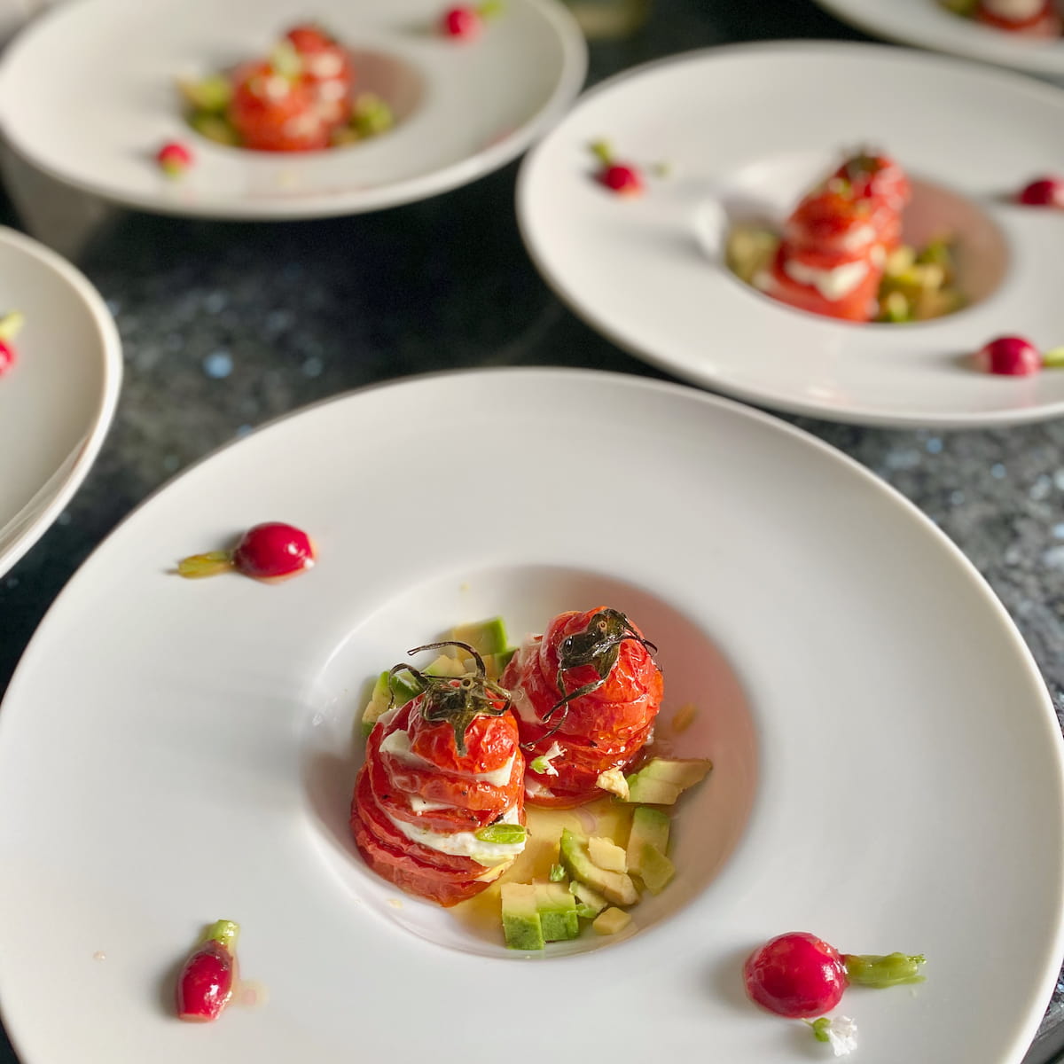 large plates filled with 2 stacked roasted tomatoes with mozzarella garnished with radishes