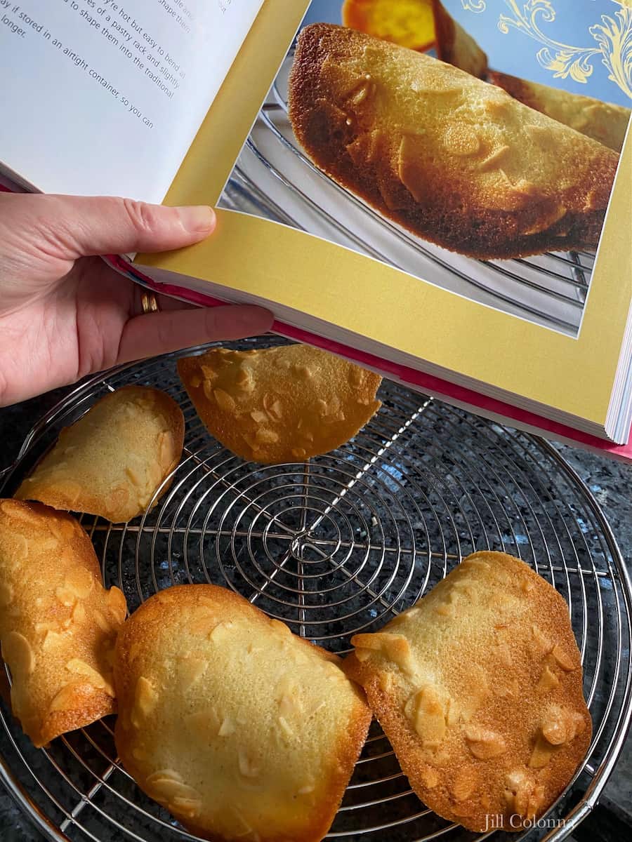 Looking at a French cookie recipe book with tuiles cooling below