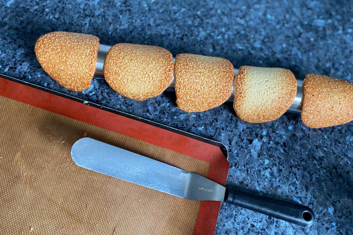 tuile cookies being shaped on a rolling pin