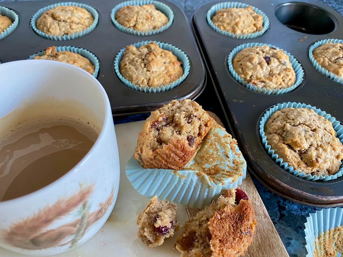 trays of healthy oat muffins just out of the oven, with one torn open with a cup of coffee