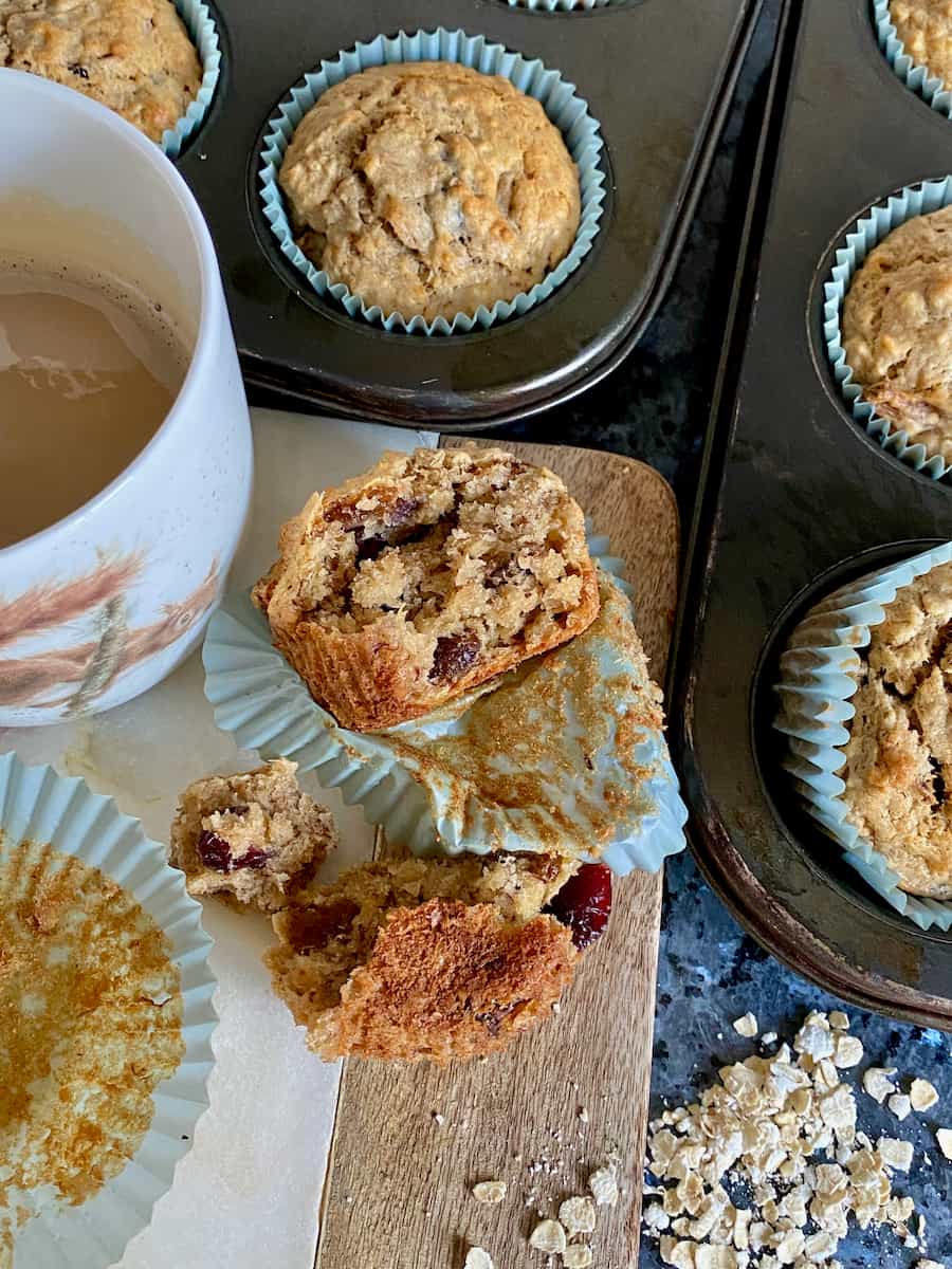 cup of coffee next to muffins in their paper cases and tins and one open to show moist fruits inside