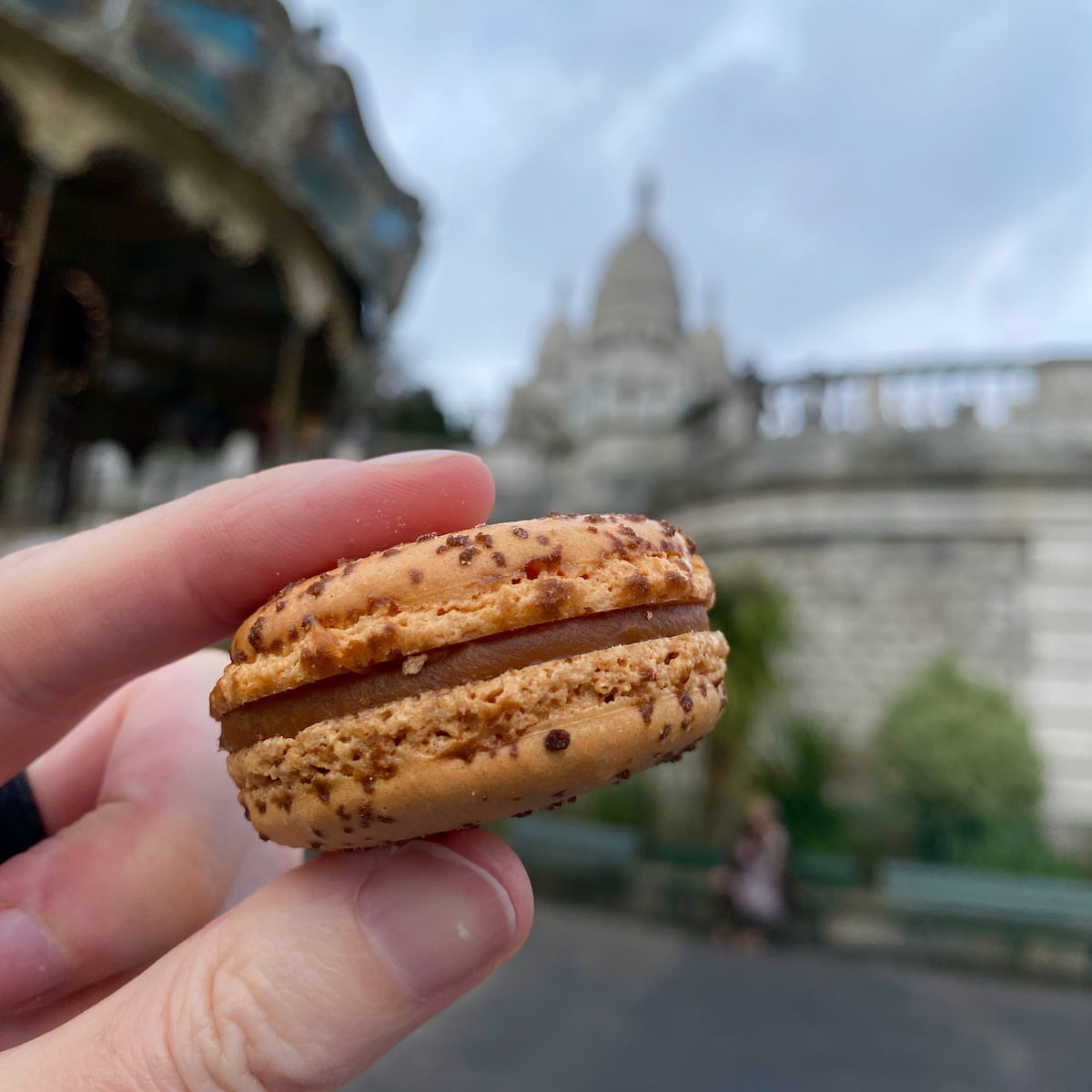 salted caramel macaron in front of a carousel and basilica of Sacre-Coeur in Paris