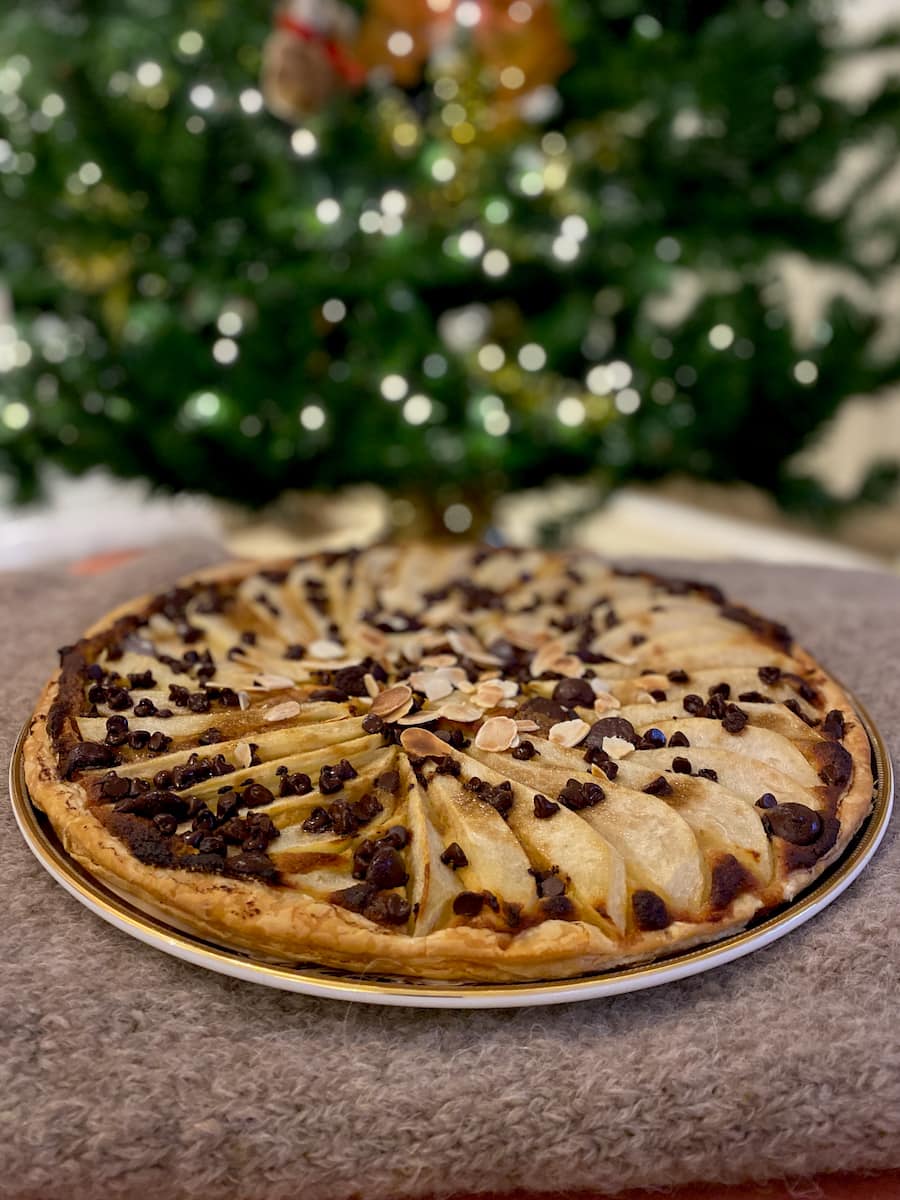 a puff pastry tart topped with pears and chocolate chips in front of a Christmas tree