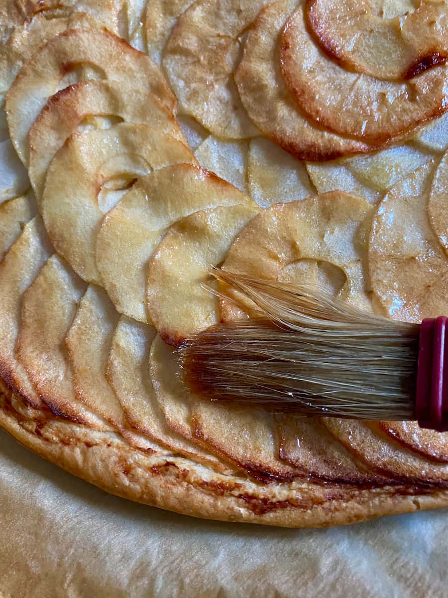 Brushing on melted apricot jam to a baked apple tart with puff pastry