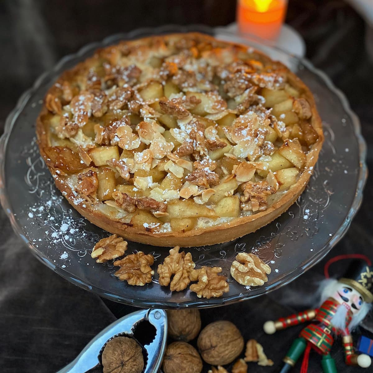 apple tart with toasted nuts on glass plate and cracking walnuts with a nutcracker doll