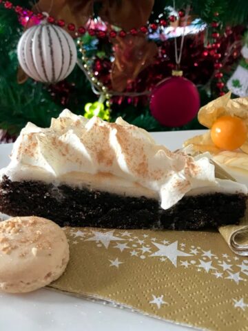 slice of chocolate cake with frosting and piped cream on plate with macaron shell and Christmas tree
