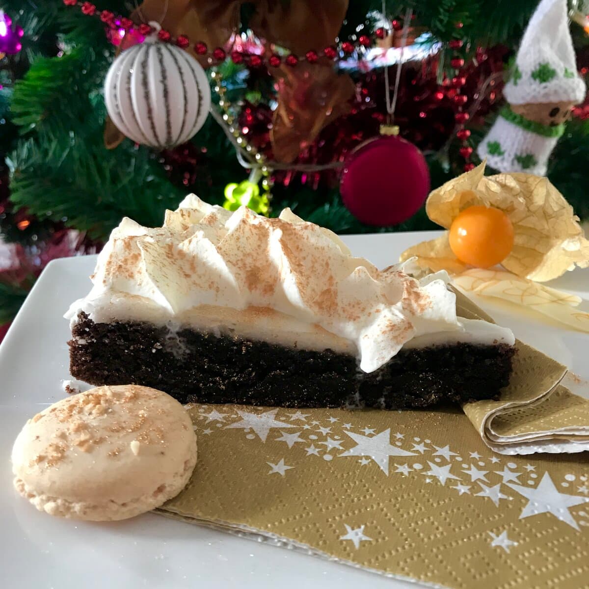 slice of chocolate cake with frosting and piped cream on plate with macaron shell and Christmas tree