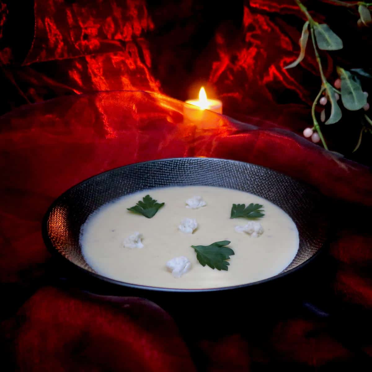 bowl of cauliflower cream soup garnished with florets, parsley and by candlelight and mistletoe