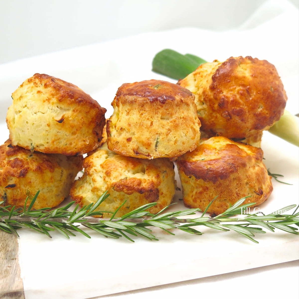 high rise cheesy scones piled on top of each other, surrounded by rosemary and spring onions