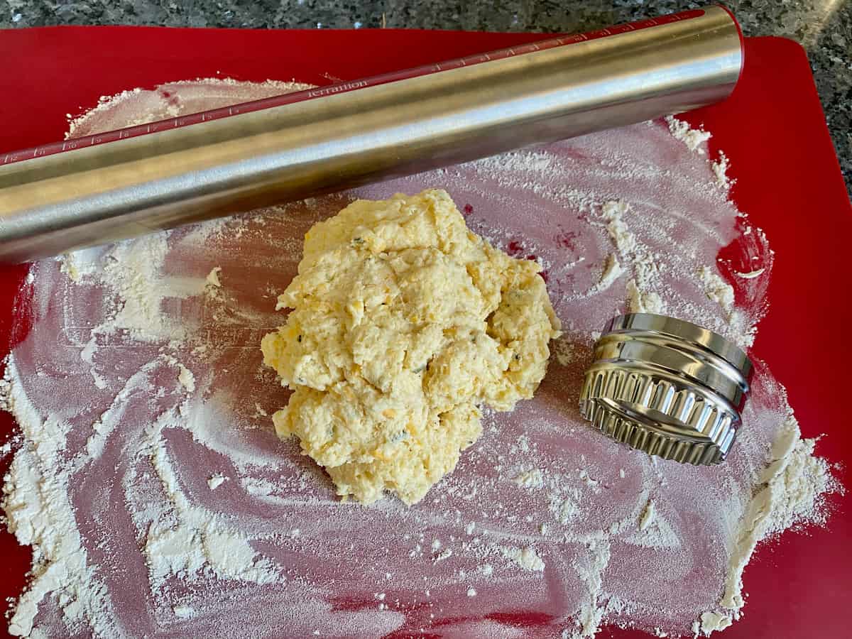 wet pile of dough on a floured surface with rolling pin and scone cutter