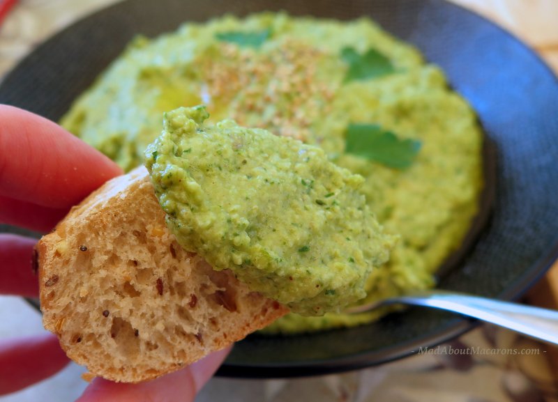 dipping a slice of French baguette into a broccoli dip of hummous