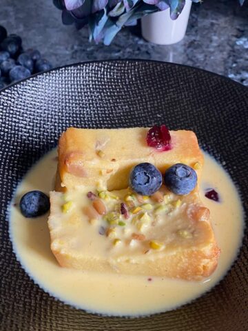 slice of pudding in a puddle of vanilla cream custard topped with nuts and berries