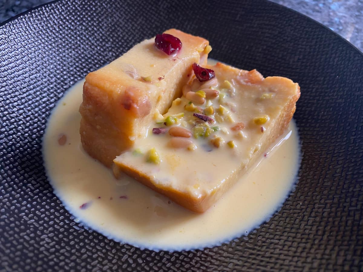 semolina cake slices on black plate in custard and topped with cranberries and nuts
