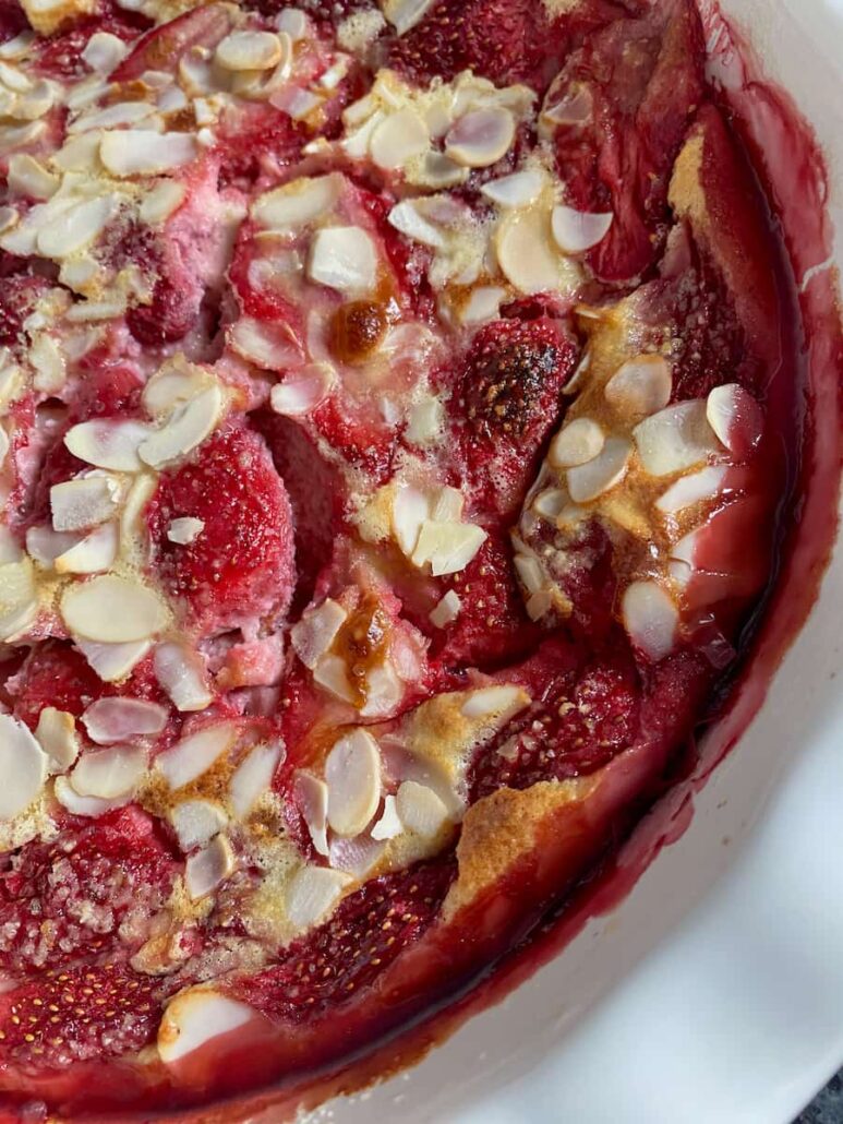 close up of baked strawberries in a custard topped with flaked almonds