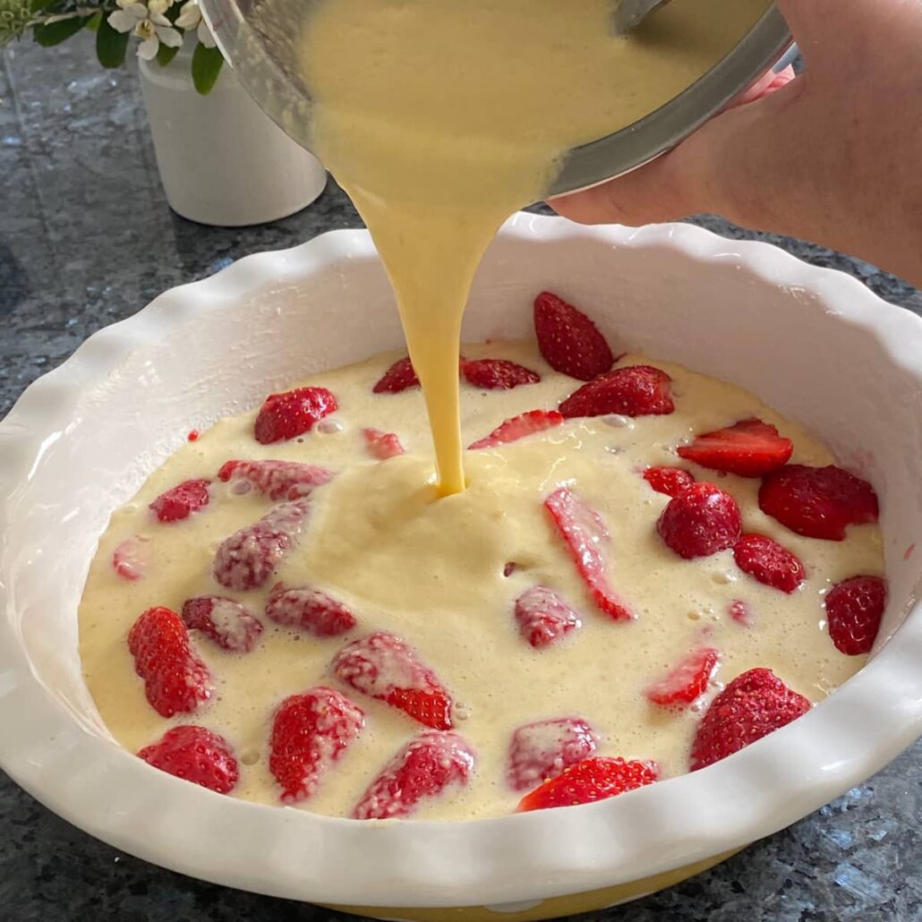 pouring custard over a dish of fresh strawberries