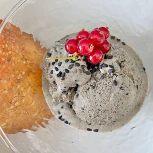 scoops of dark grey ice cream topped with black sesame seeds and redcurrants, served with a sesame tuile cookie