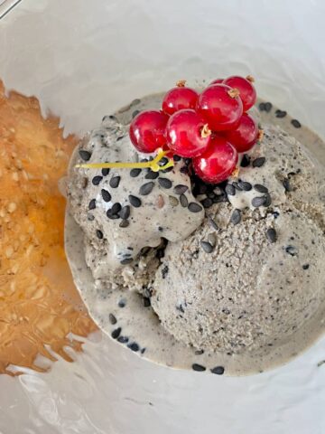 scoops of dark grey ice cream topped with black sesame seeds and redcurrants, served with a sesame tuile cookie