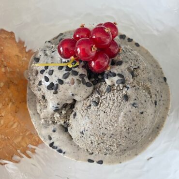 glass dish with scoop of black sesame ice cream topped with redcurrants and tuile
