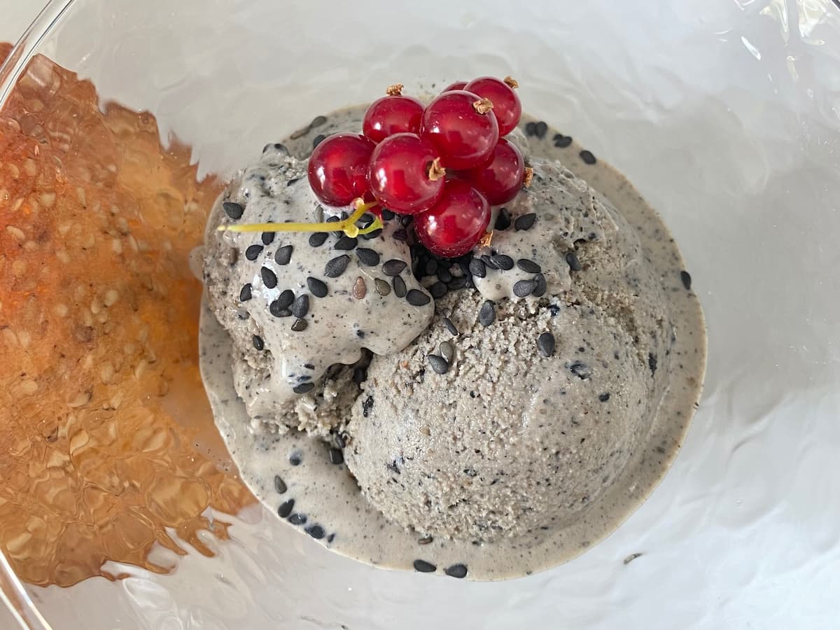 glass dish with scoop of black sesame ice cream topped with redcurrants and tuile