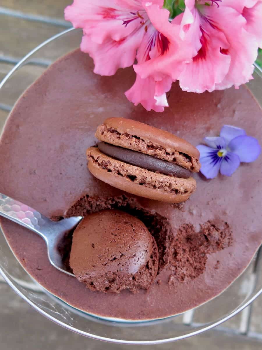 spoonful of a fluffy dark chocolate dessert topped with a macaron and edible flower