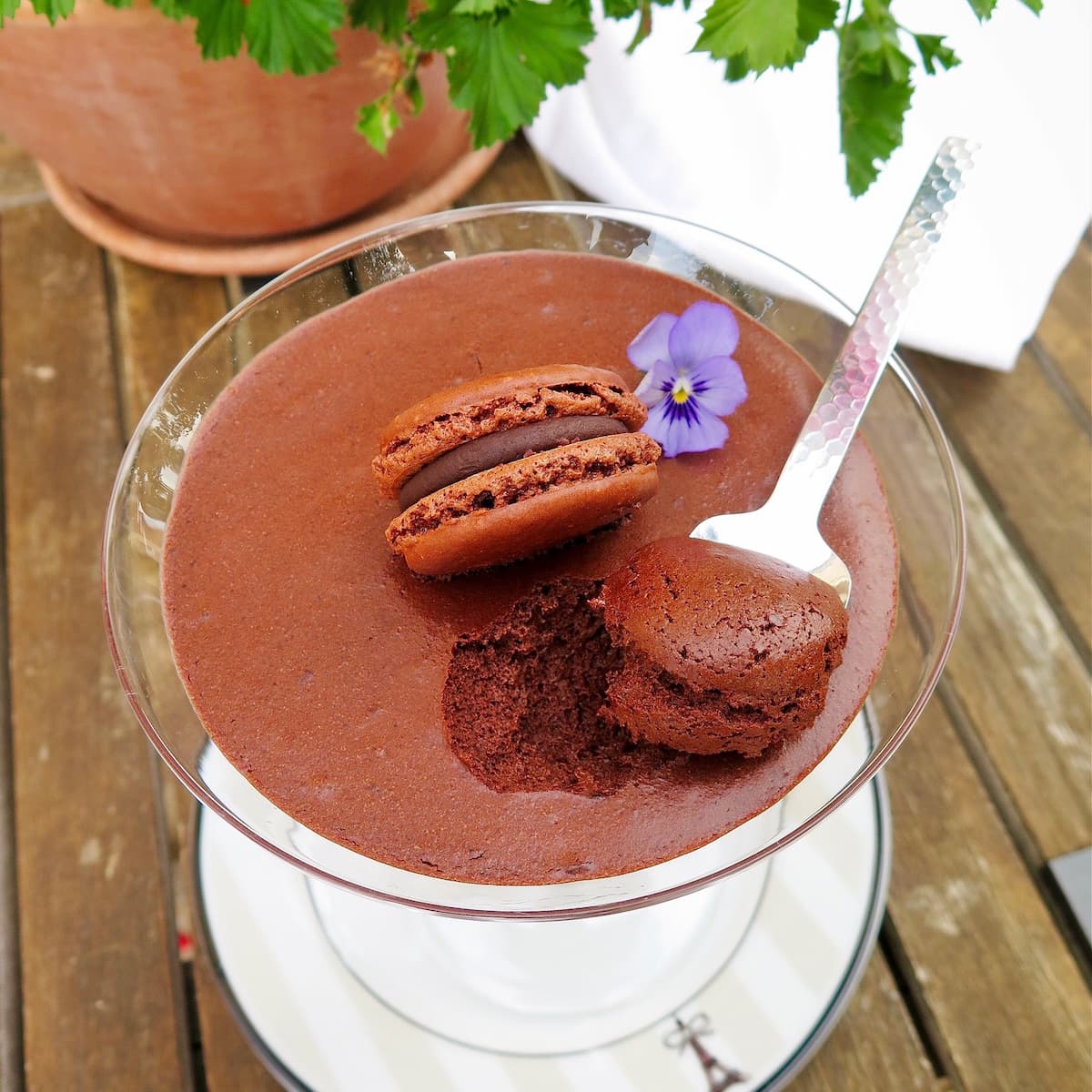spoonful of chocolate mousse with a chocolate macaron on top and edible pansy